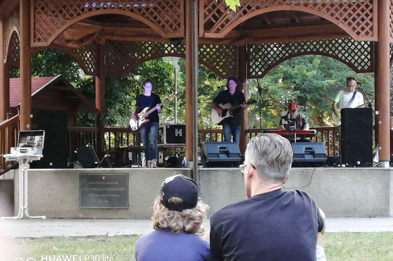 Vater uns Sohn sitzen auf dem Rasen und hören einer Band beim Picknick im Park 2020 zu.