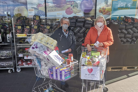 2 Frauen mit Einkaufswägen voller Spenden vor einem Supermarkt.