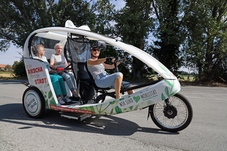 2 ältere Personen sitzen mit der Pilotin in der Rikscha 
