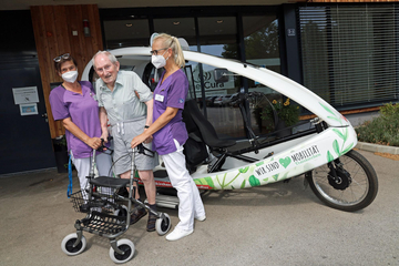 Ein Senior und zwei Pflegekräfte vor dem Dreiradler
