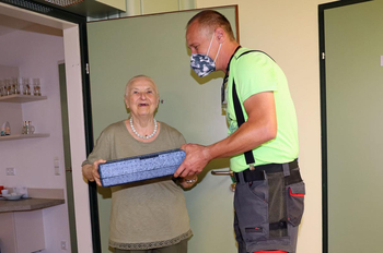 Mitarbeiter übergibt einer Seniorin das Essen