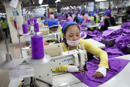 Eine junge Frau beim Arbeiten an einer Nähmaschine in einer Fabrikshalle in Asien.