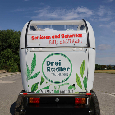 Die Fahrradrikscha von hinten mit der Aufschrift: "Senioren und Senoritas bitte einsteigen"