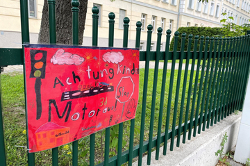 Ein Schild mit der Aufschrift "Achtung Kinder, Motor aus!" am Zaun der VS Traiskirchen
